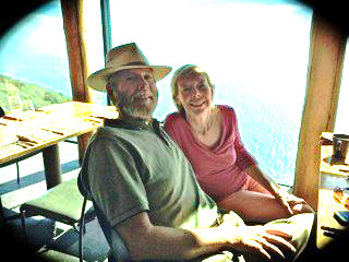 Ed and Barbara sitting indoors while over looking the ocean