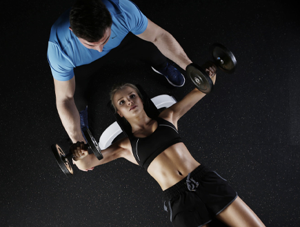 Woman bench pressing some dumbbell while a guy spots her.
